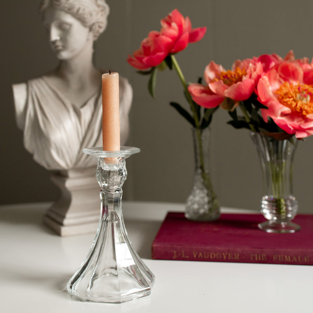 Vintage crystal candlestick holding a candle in front of peonies and a bust.