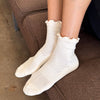 White ruffled socks worn by a person sitting on a brown couch.