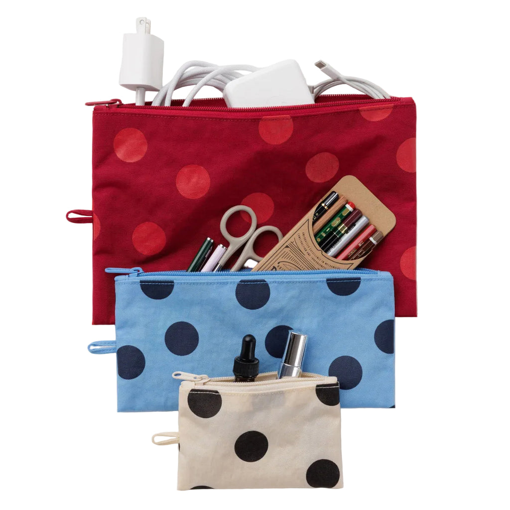 Three fabric zip pouches with polka dots are arranged on a light gray background. The top pouch is red with red polka dots and contains white charging accessories.
