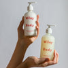 Two bottles of Wiley Body lotion held by a person against a plain background