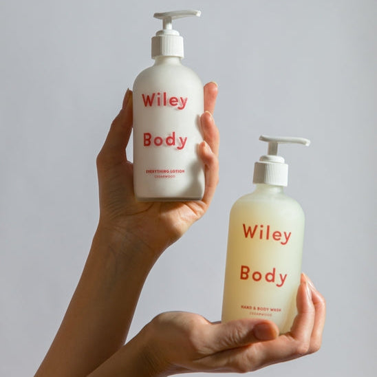Two bottles of Wiley Body lotion held by a person against a plain background