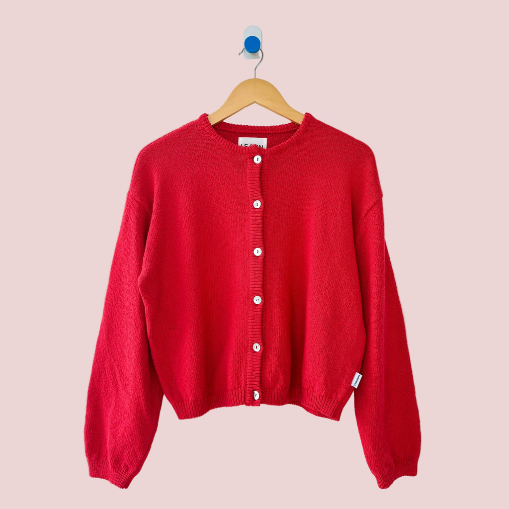 Red cardigan on a wooden hanger against a white background