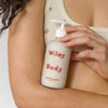 Person holding a bottle of 'Wiley Body' lotion against a neutral background