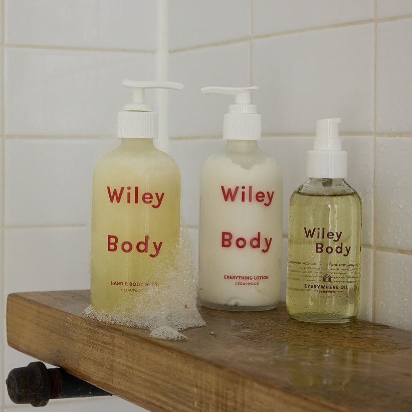 Three bottles of 'Wiley Body' products on a wooden shelf against a tiled wall.
