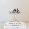 Vintage glass pedestal candy dish holding fresh figs and sitting atop a stack of vintage books.