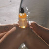 Hand holding a bottle of 'High Noon' body oil with a blurred background