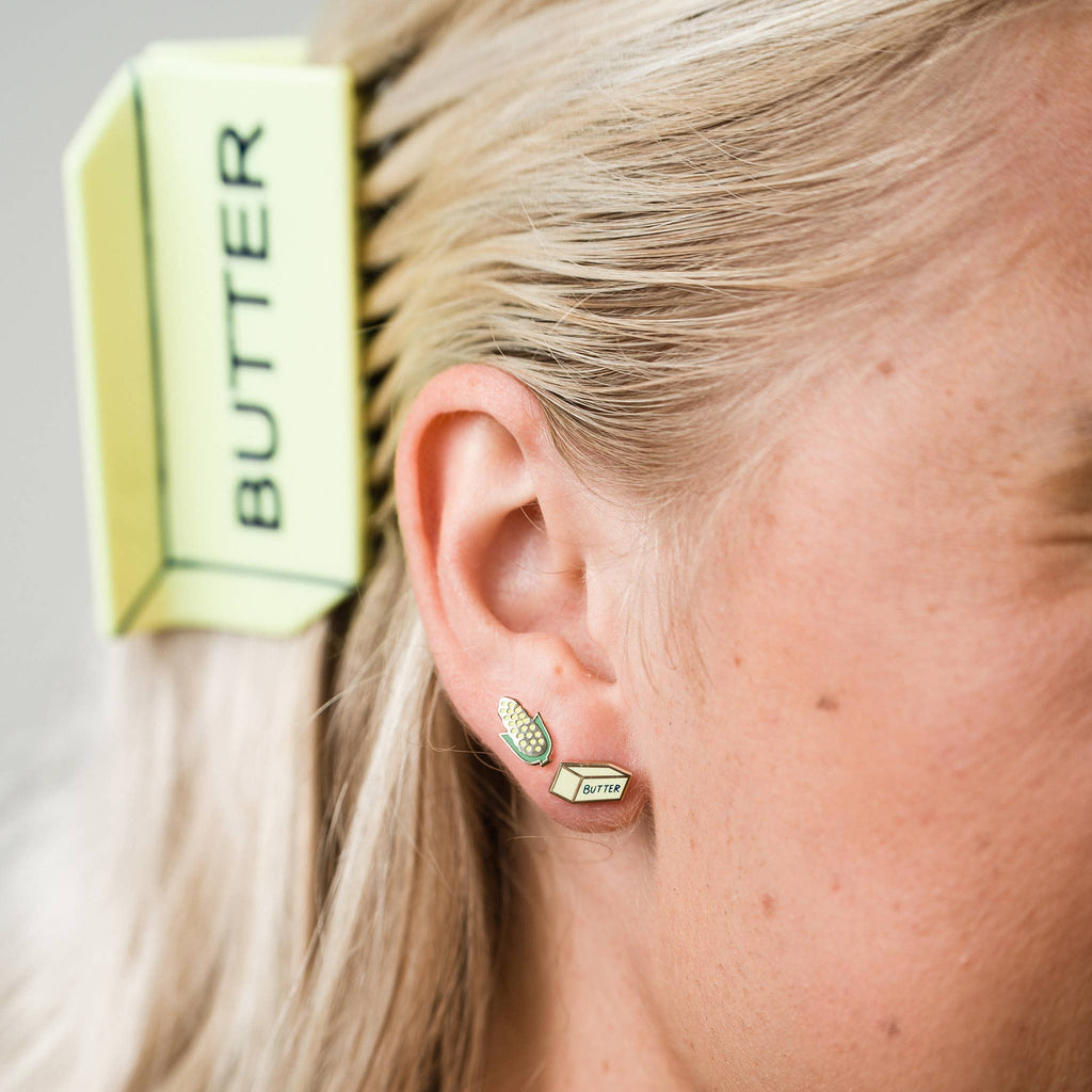 Close-up of a person wearing gold earrings with 'BUTTER' branding, with a bar of butter claw clip  in the background.