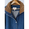 A close-up of a blue denim button-front jacket with a brown corduroy collar, hanging on a wooden hanger against a light gray background. The brand label reads 'LE BON SHOPPE'.