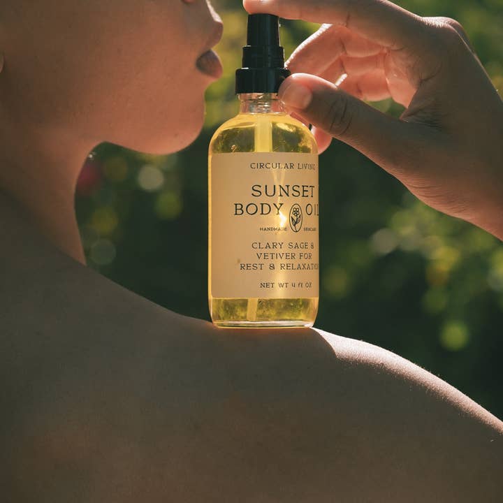 Person holding a bottle of 'Sunset Body Oil' with a blurred green background
