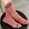 A pair of ribbed crew socks in a dusty rose pink color with black stripes, worn on a person's feet and resting on a black stool. The brand name 'LE BON SHOPPE' is printed in black on the sole of one sock.