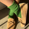 Person wearing green socks and tan moccasins on a concrete floor.