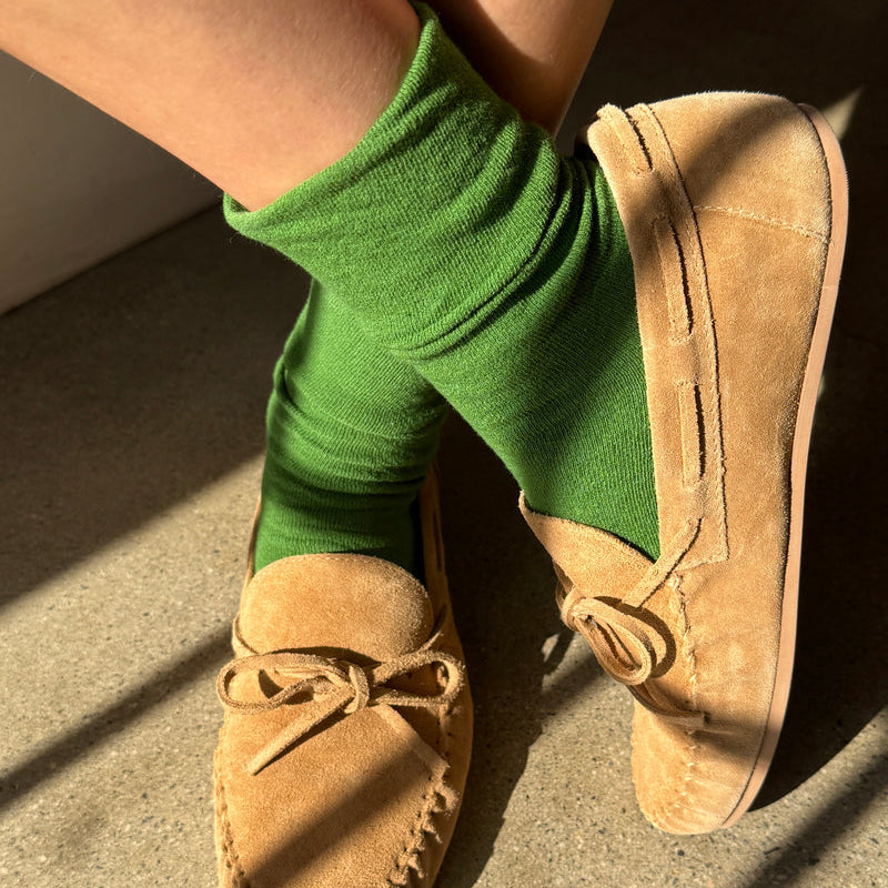 Person wearing green socks and tan moccasins on a concrete floor.