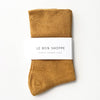 Pair of mustard yellow socks with a white label on a light beige background