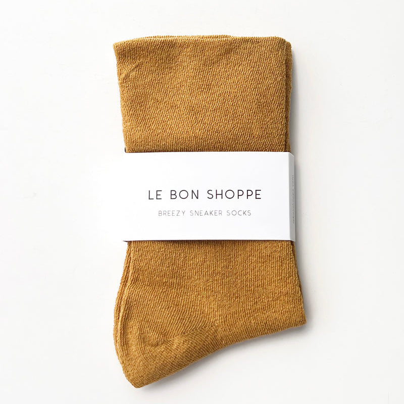 Pair of mustard yellow socks with a white label on a light beige background