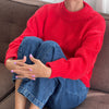 Person wearing a red sweater, blue jeans, and checkered shoes sitting on a brown couch.