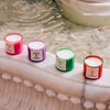 Four colorful Roen candles on a marble ledge with water in the background