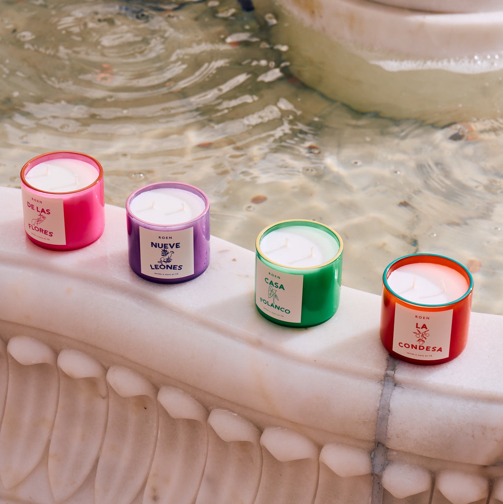 Four colorful Roen candles on a marble ledge with water in the background