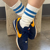 Navy blue sneakers with orange accents worn with white socks featuring blue stripes.