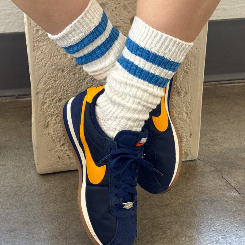 Navy blue sneakers with orange accents worn with white socks featuring blue stripes.
