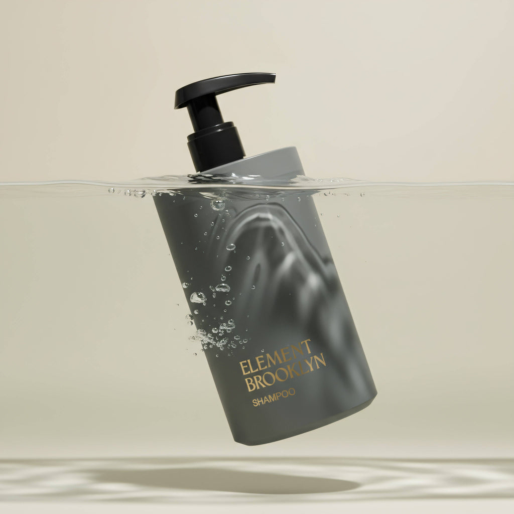 Shampoo bottle labeled 'Element Brooklyn' with a pump mechanism, partially submerged in water on a beige background.