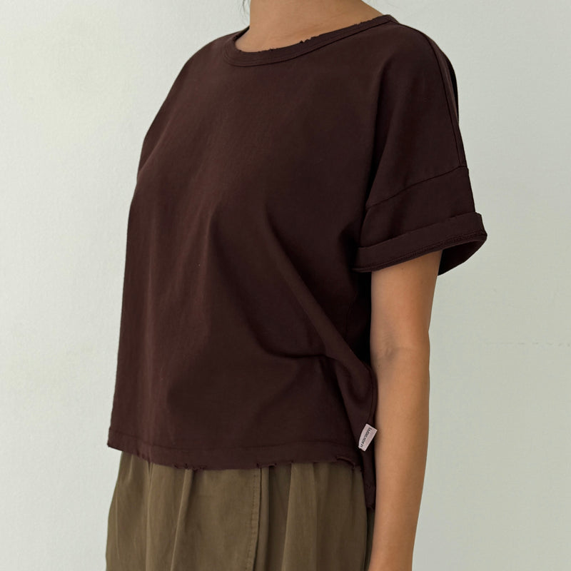 Person wearing a brown oversized t-shirt and green pants against a plain background