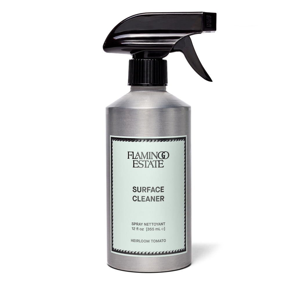 A 12 fl oz metal spray bottle of Flaming Estate Surface Cleaner in Heirloom Tomato, featuring a brushed silver body, a black trigger spray top, and a pale mint-green label with black text.