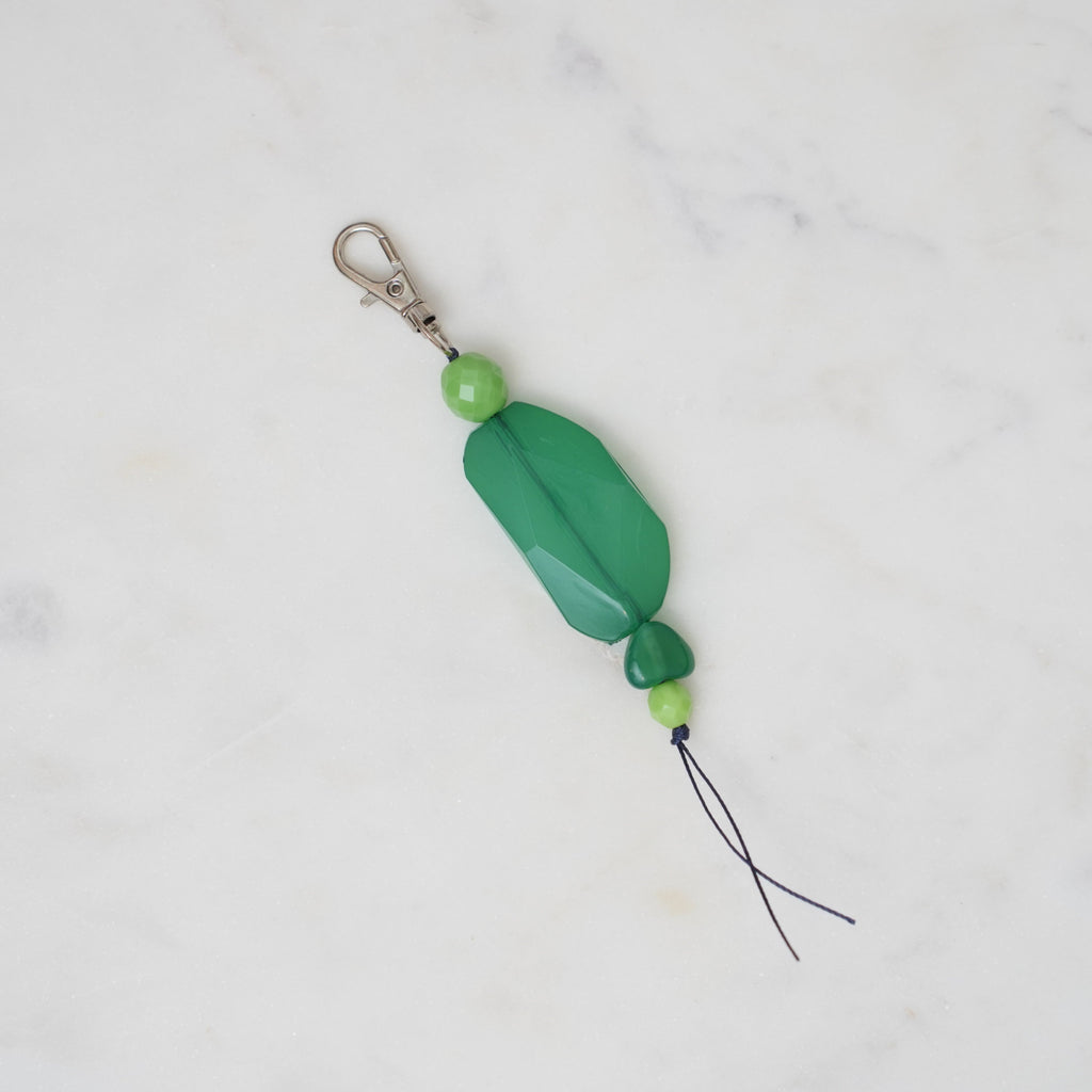 Green bead charm on a white marble background