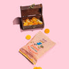 Wooden treasure chest with orange gummy coins and a package labeled 'Pippi Longstocking' on a pink background.