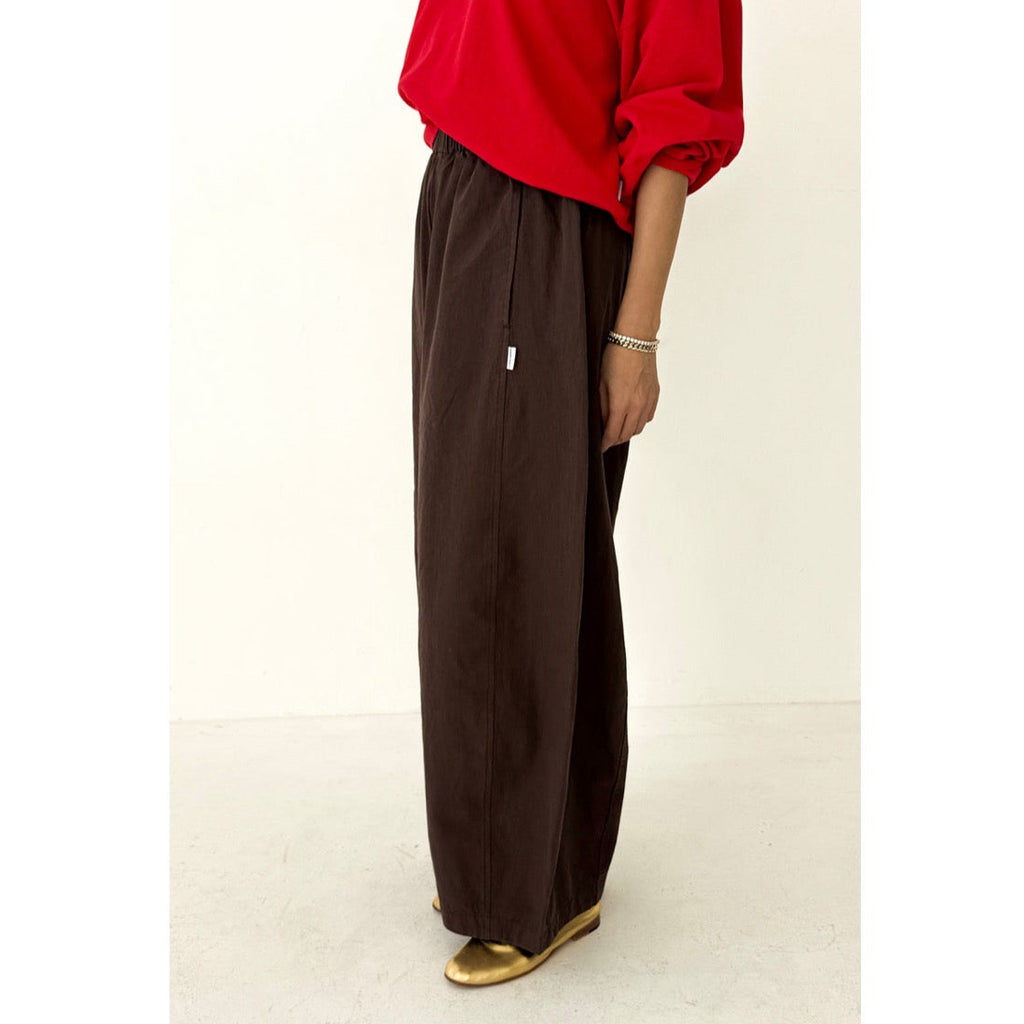 Person wearing a red top and brown wide-leg pants on a white background