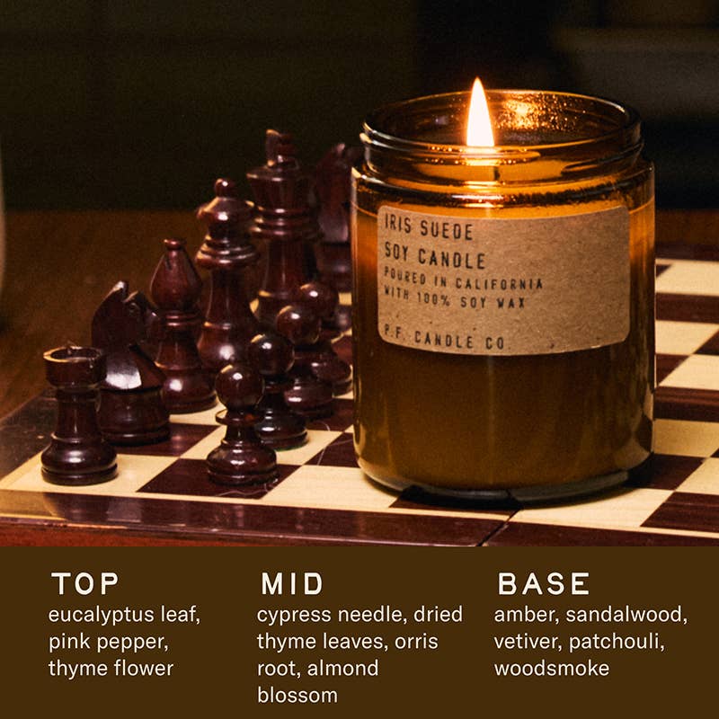 Scented candle in a glass jar on a chessboard with chess pieces, featuring a label and fragrance description.