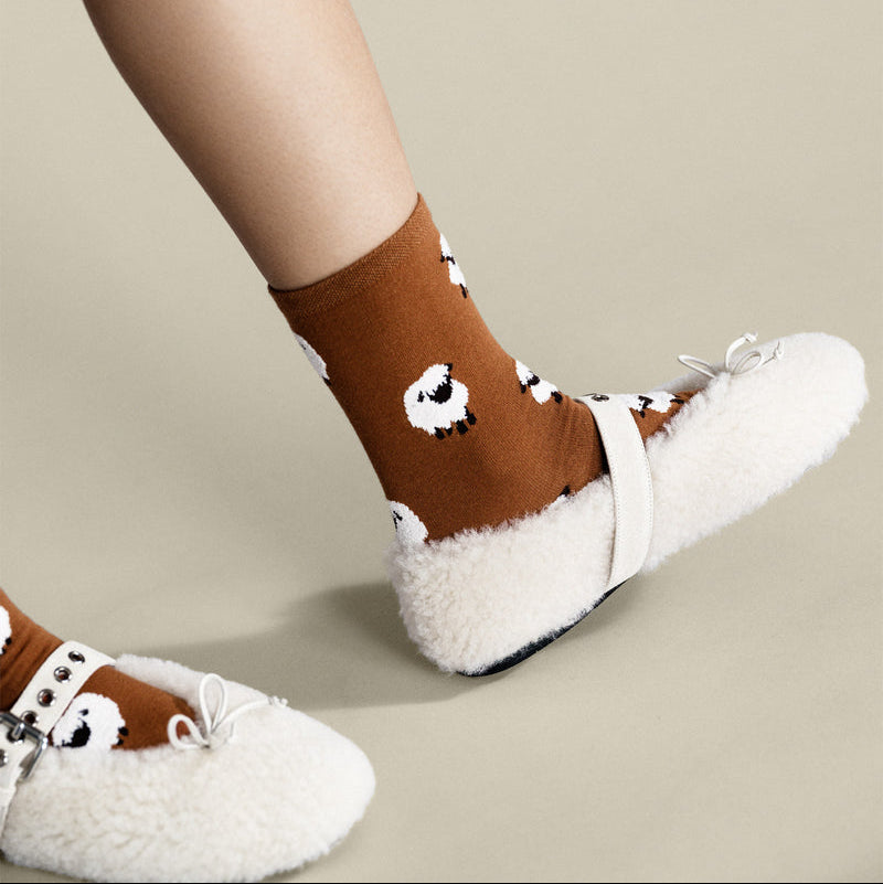 Brown socks with white sheep design and white fuzzy slippers on a beige background