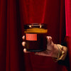 Hand holding a Smoked Cherry candle against a red curtain background
