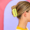 Person with a yellow butter claw clip in their hair against a colorful background