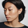 Person with short black hair wearing a dark top against a plain background