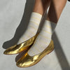White socks with yellow stripes and gold flats on a light gray background