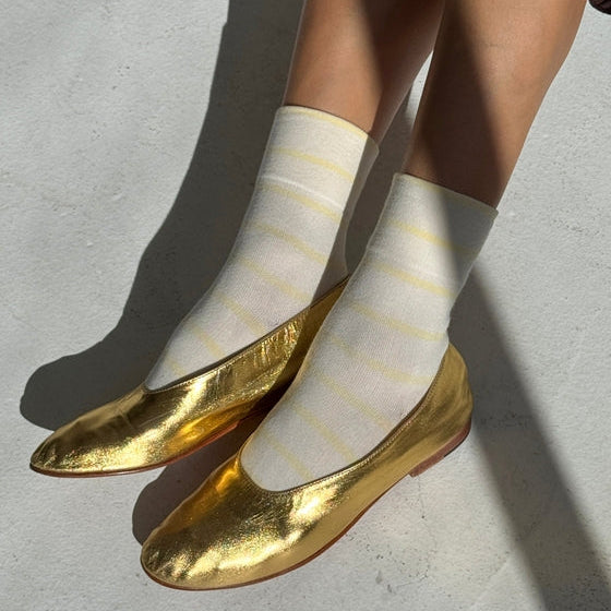 White socks with yellow stripes and gold flats on a light gray background