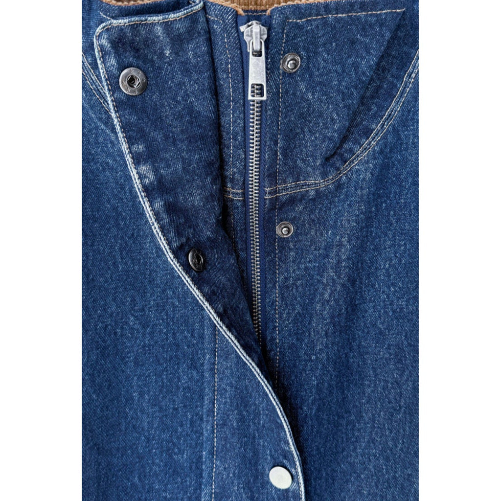 Close-up of a blue denim garment featuring a central silver zipper, metal snap buttons, and contrast white stitching on a plain white background.