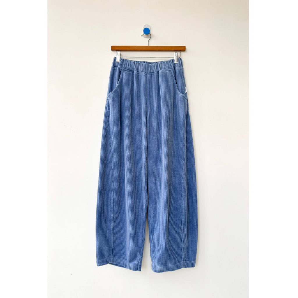 Blue denim pants hanging on a wooden hanger against a white background