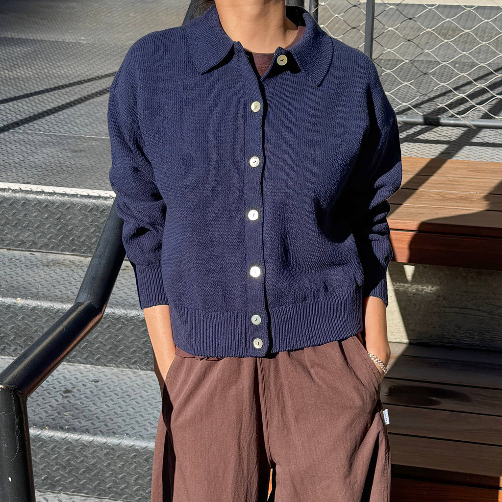 Person wearing "The Club" navy blue cardigan and brown pants standing on steps.