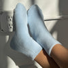 Light Celeste blue Le Bon Shoppe Cloud socks being worn on a white surface with a power outlet.