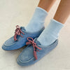Blue suede loafers with red laces worn with light blue Le Bon Shoppe Cloud socks on a neutral background
