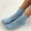 Light blue socks with ruffled top worn by a person on a light gray background