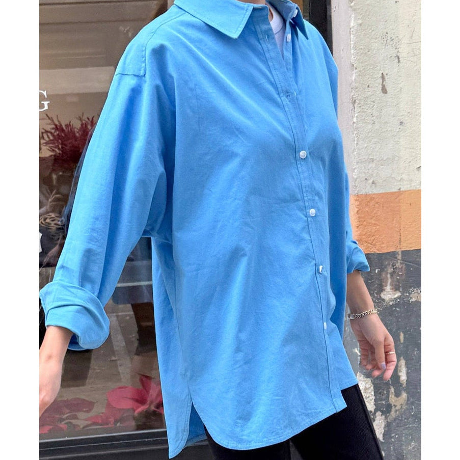 Person wearing a light blue shirt with rolled-up sleeves, standing against a blurred background.