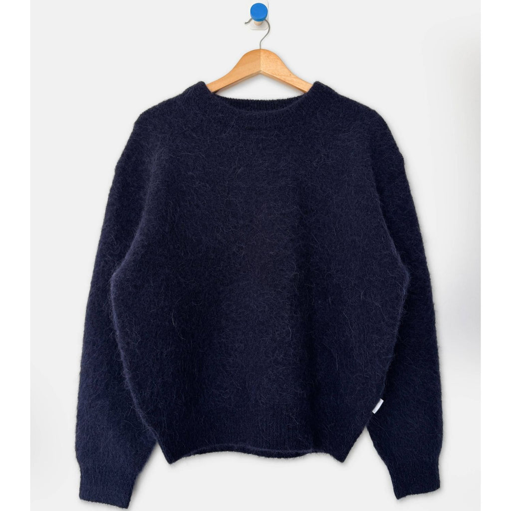 A dark navy blue fuzzy knit sweater hanging on a wooden hanger with a blue hook against a plain white background.