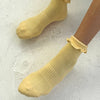 Yellow socks with ruffled top worn by a person on a light gray background