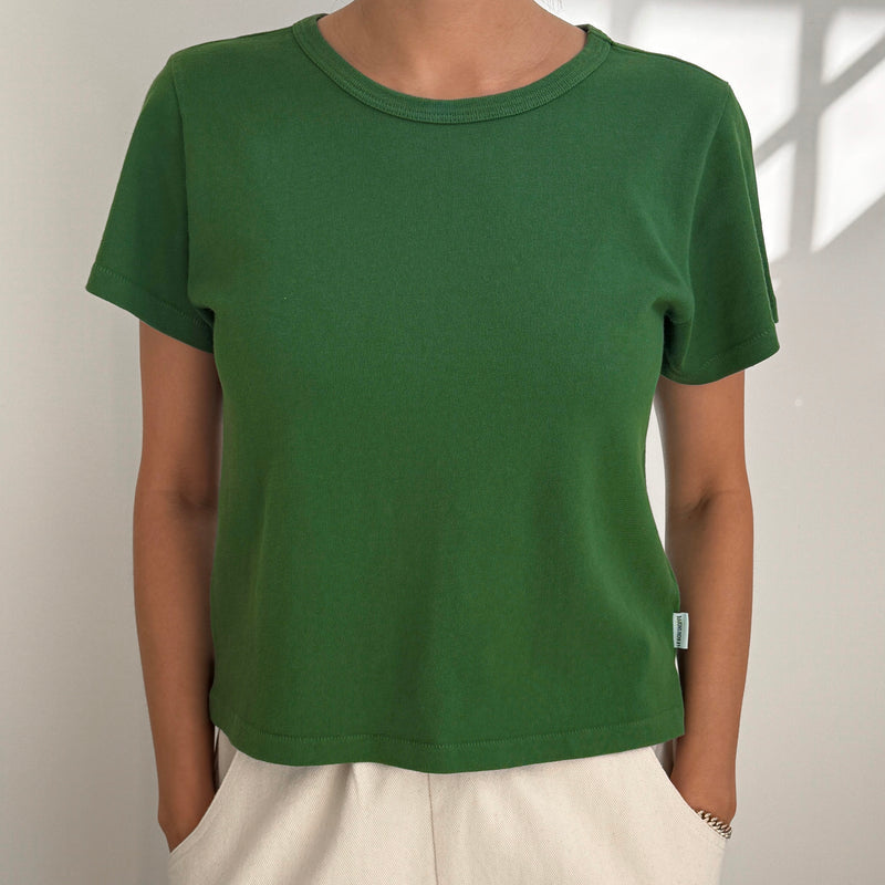 Person wearing a green t-shirt and beige pants against a plain background