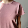 Person wearing a pink t-shirt and white pants against a neutral background