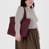 Person wearing a maroon quilted bag on a white background