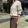 Person wearing a beige sweater and brown pants on a city street.