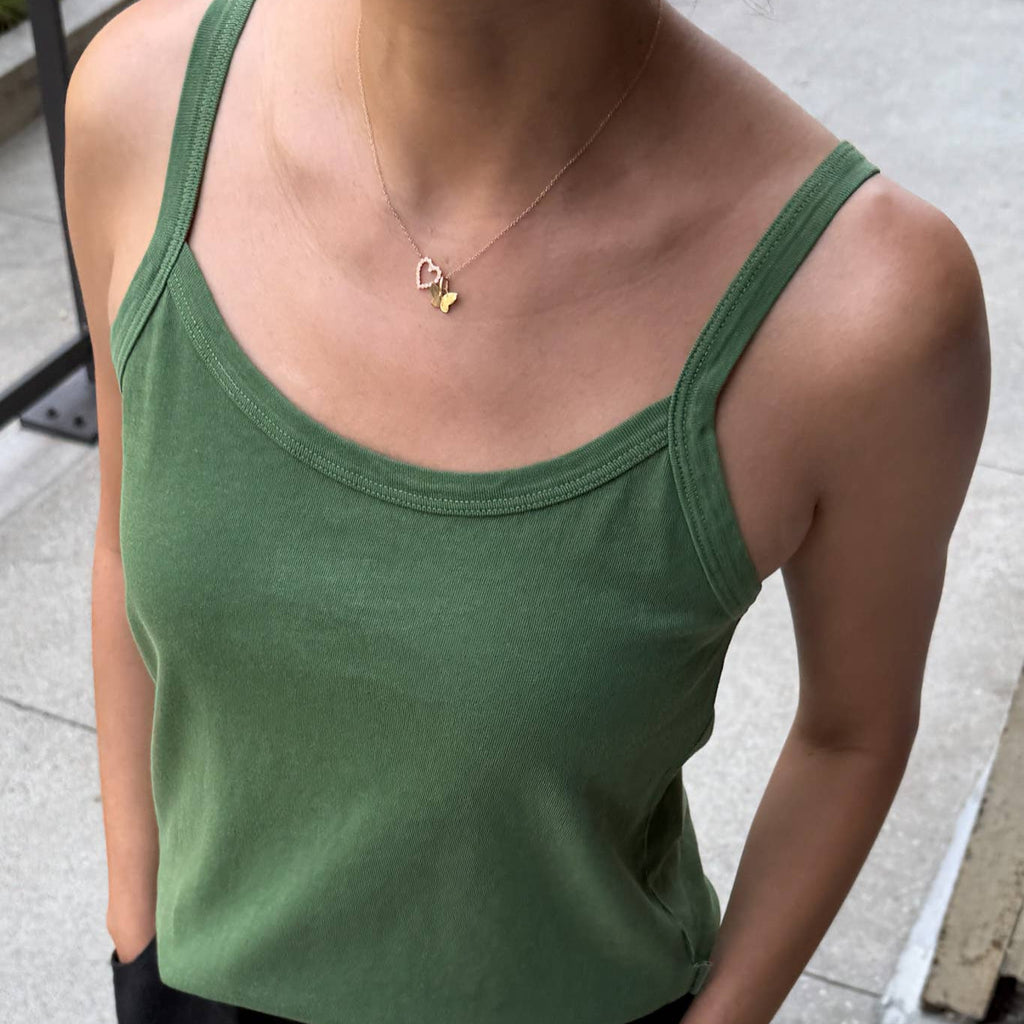 Person wearing a green tank top and black pants on a sidewalk.